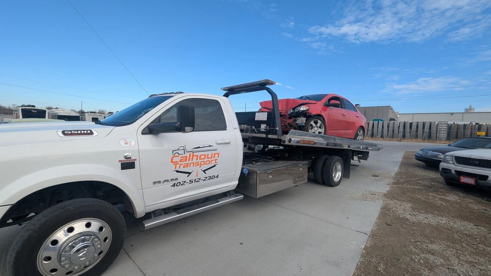 Red sedan with front-end damage loaded on a Calhoun Transport flatbed after an accident recovery