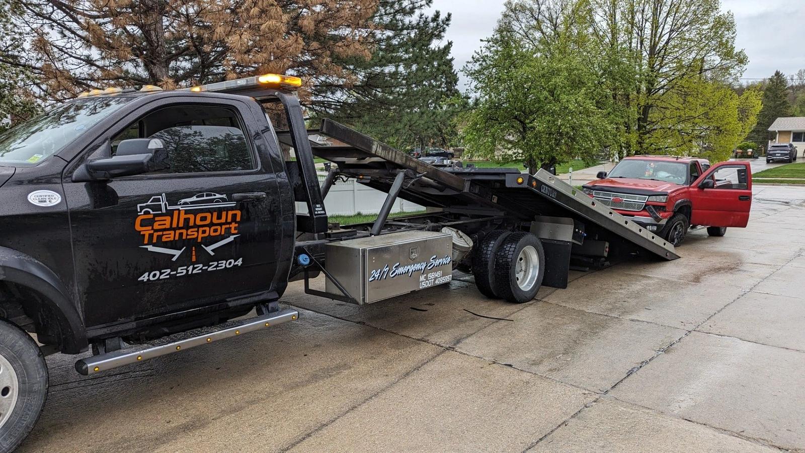 Calhoun Transport flatbed tilting its deck to load a red pickup from a residential driveway