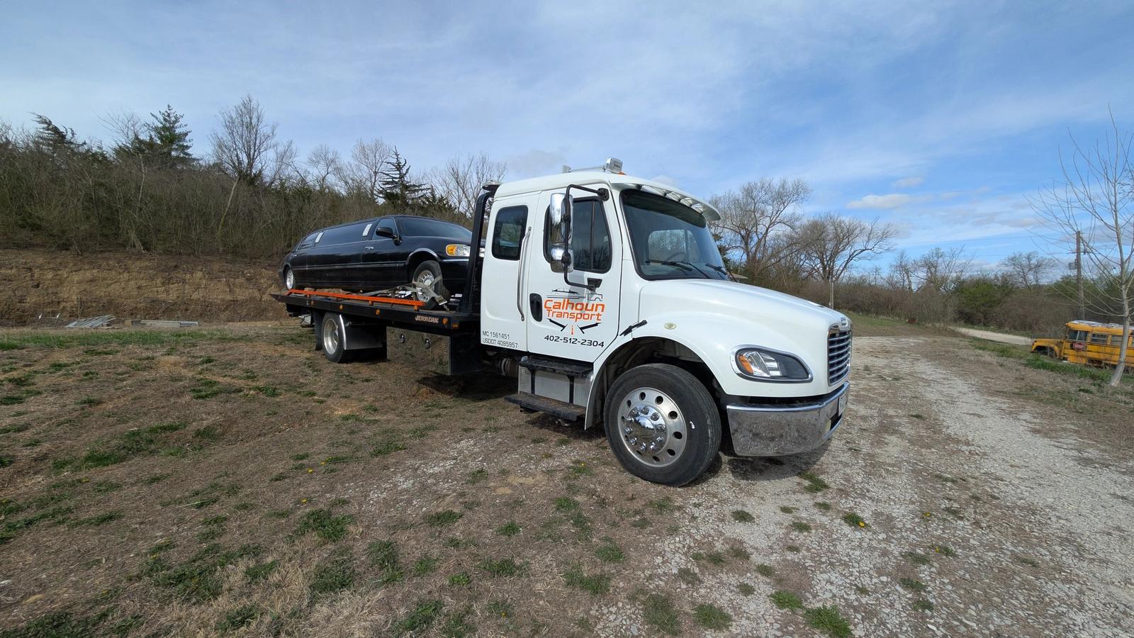 Calhoun Transport flatbed tow truck hauling a black limousine on a rural Nebraska road