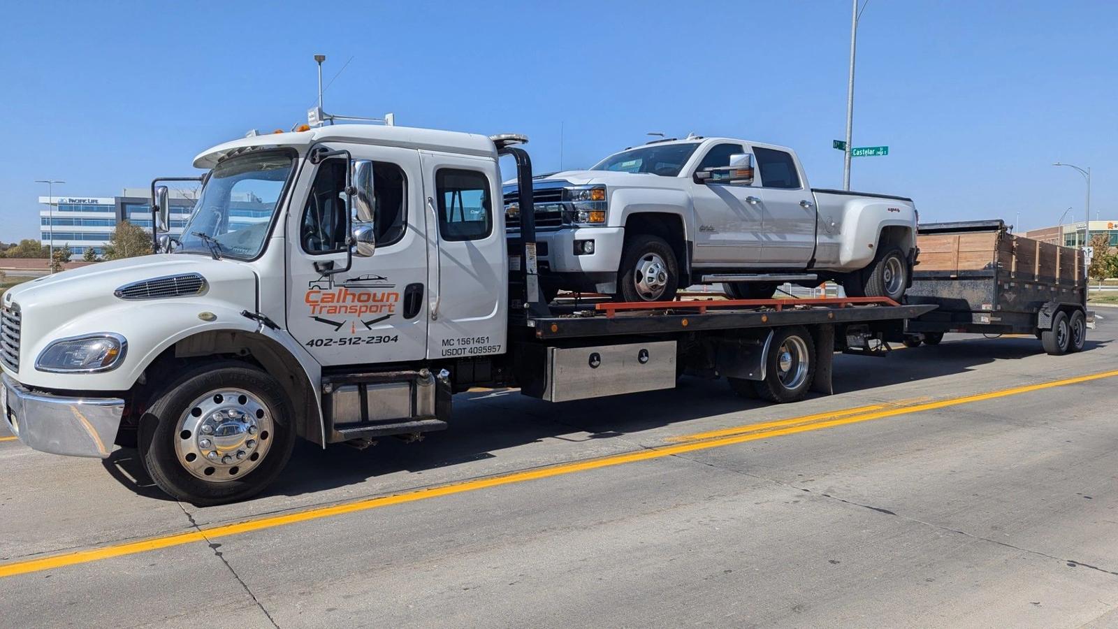 Calhoun Transport flatbed towing a dually pickup and dump trailer on a Nebraska highway