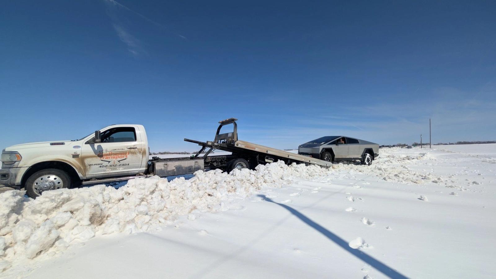Calhoun Transport flatbed recovering a Tesla Cybertruck stuck in a snow-covered field in rural Nebraska